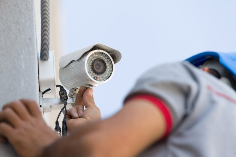 A technician performs maintenance on an exterior security camera.